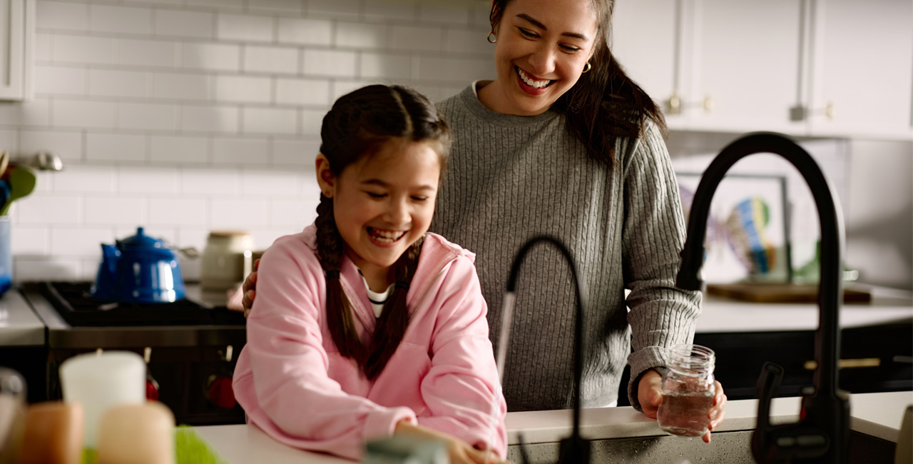 Mom and Daughter washing fruit with Kinetico water in kitchen sink.